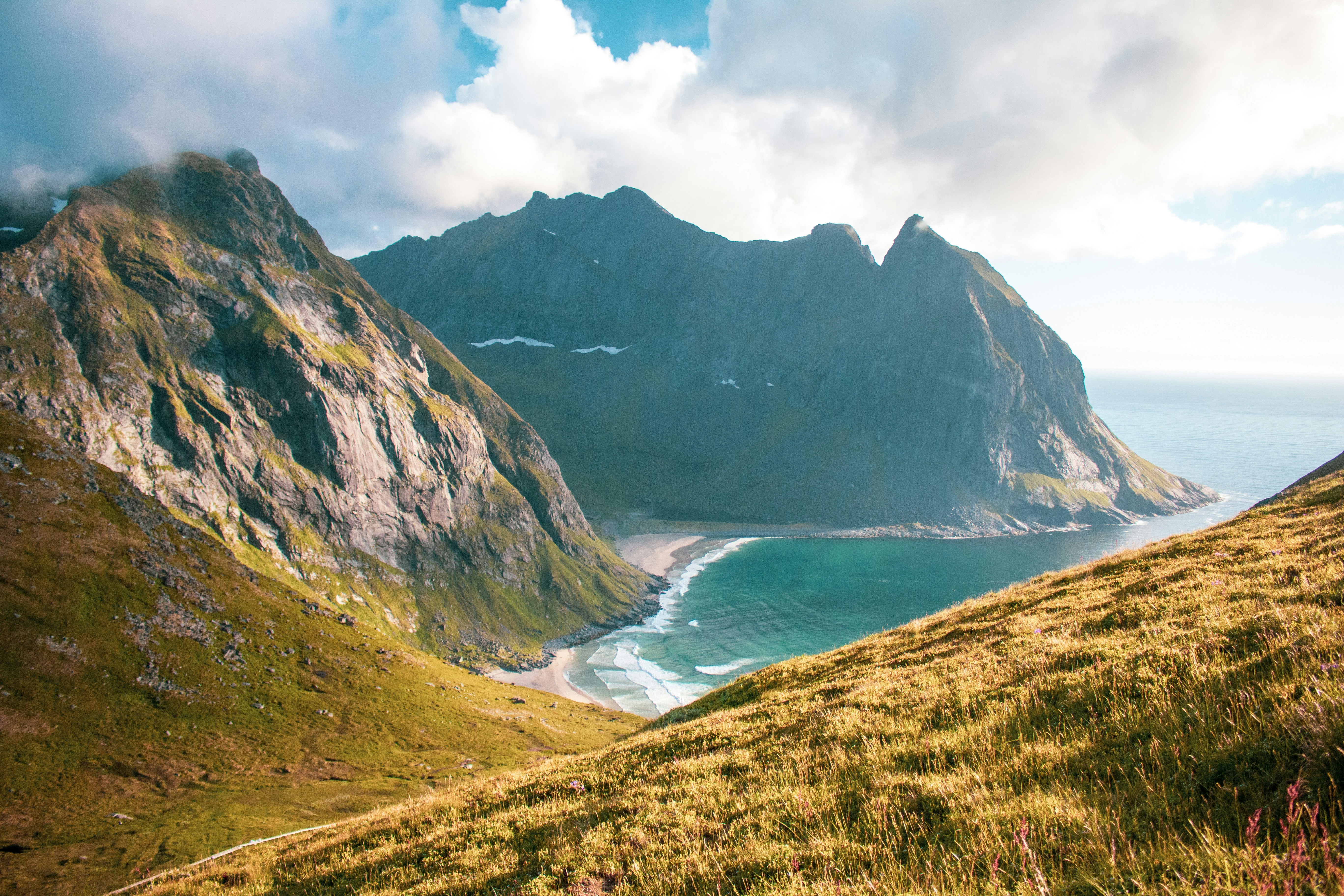 A view from the top of a mountain, down the mountainside to the beach below, where the sea is rolling in